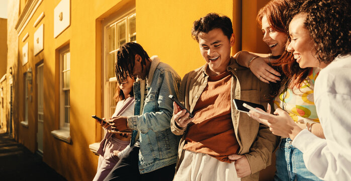 Group of friends sharing happy moments with smartphones on sunny day