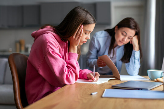 Upset mother and teen daughter studying at home, girl doing school assignments, difficult task, routine boring homework, strict mother controlling schoolgirl
