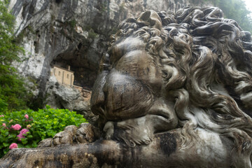 Entrance to the Covadonga cave and hermitage, framed by lush greenery and a lion statue in Asturias, Spain