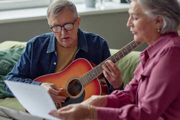 Portrait of senior man playing guitar and reading lyrics while singing song enjoying music at home