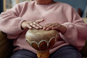 Close up of unrecognizable Black senior woman playing traditional drum while enjoying music and...