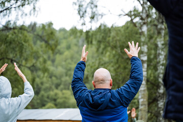 In a natural setting, a joyous group of individuals are seen lifting their arms, standing on the grass, under a clear sky. Their pose reflects happiness and a sense of liberation