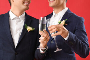 Married gay couple with glasses of champagne on red background