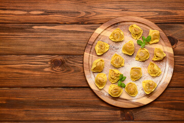 Board with raw dumplings and basil on wooden background
