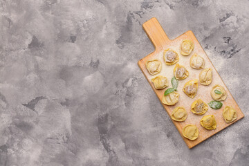 Wooden board with raw dumplings and basil on grey background