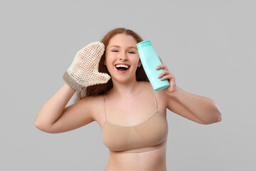 Beautiful young happy woman with bath massage mitten and bottle of shower gel on grey background