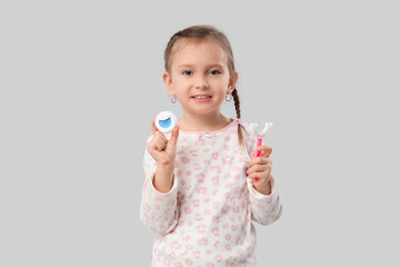 Happy little girl with toothbrush and dental floss on grey background