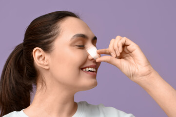 Fototapeta premium Happy young woman with bandaged nose on lilac background. Plastic surgery concept