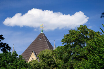 a  cloud over the roof with the david star of the cologne synagogue behind the trees of rathenauplatz