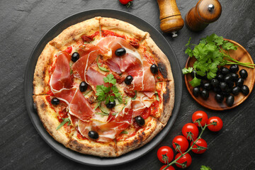 Tasty pizza with cured ham, olives, tomatoes and parsley on black table, top view