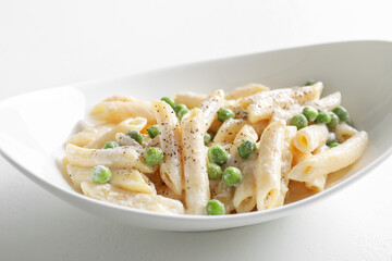 Delicious pasta with green peas and creamy sauce in bowl on white table