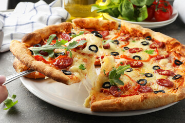 Taking piece of tasty pizza with smoked sausages, olives, pepper and parsley at gray table, closeup