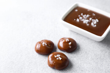 Tasty candies, caramel sauce and salt on light grey table, space for text