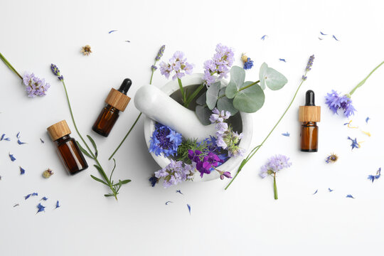 Aromatherapy. Essential oils, flowers, eucalyptus leaves, mortar and pestle on white background, flat lay