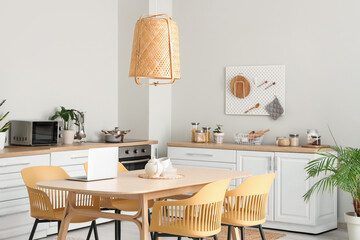 Interior of modern kitchen with white counters, dining table, laptop, chairs and lamp
