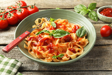 Delicious pasta with tomato sauce, basil and fork in bowl on wooden table, closeup