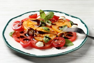Tasty salad with balsamic vinegar, mozzarella and fork on white wooden table, closeup