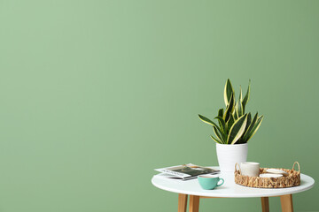 Coffee table with magazine, cup of tea and plant near green wall in room