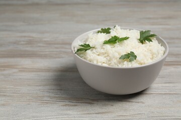 Tasty cooked rice with parsley in bowl on wooden table. Space for text