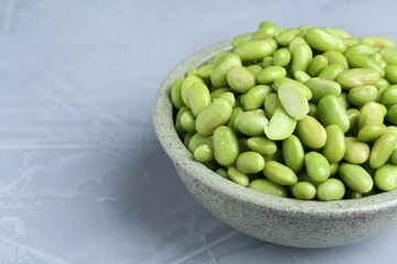 Fresh edamame soybeans in bowl on grey textured table, closeup. Space for text