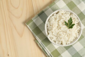 Delicious boiled rice in bowl and parsley on wooden table, top view. Space for text