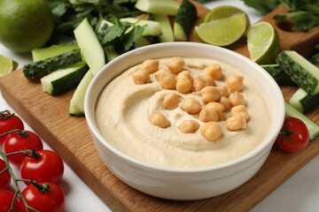 Tasty hummus with chickpeas in bowl and fresh products on light table, closeup