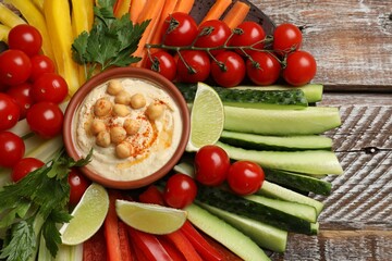 Tasty homemade hummus served with different vegetables on wooden table, top view