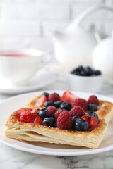 Tasty puff pastries with berries and tea on white marble table, closeup