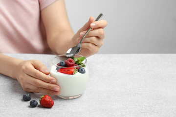 Woman eating tasty yogurt with fresh berries at light gray textured table, closeup. Space for text © New Africa