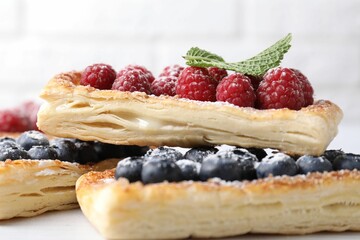 Tasty puff pastries with berries on white wooden table, closeup