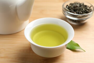 Refreshing green tea in cup, teapot and leaves on wooden table, closeup