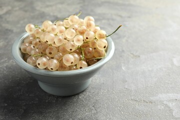 Fresh white currant berries in bowl on gray textured table, closeup. Space for text