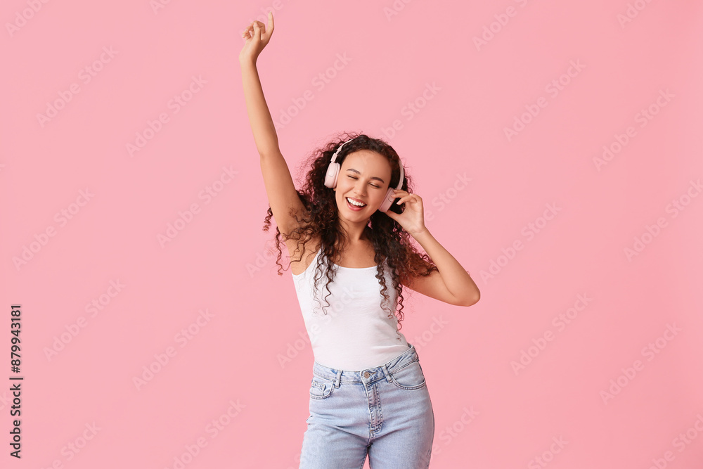 Poster Happy young African-American woman in headphones dancing on pink background