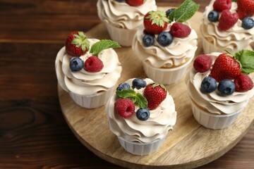 Tasty cupcakes with different berries and mint on wooden table, closeup