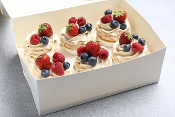 Tasty cupcakes with different berries in box on light grey table