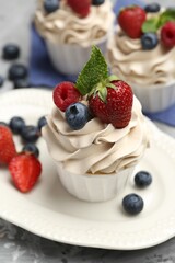 Tasty cupcakes with different berries and mint on light grey table, closeup