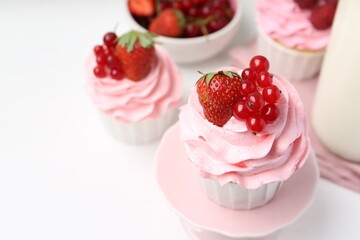 Tasty cupcakes with strawberries and red currants on white table, closeup. Space for text