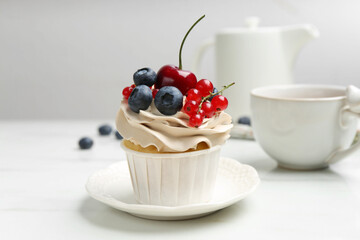 Tasty cupcake with different berries and tea on white marble table