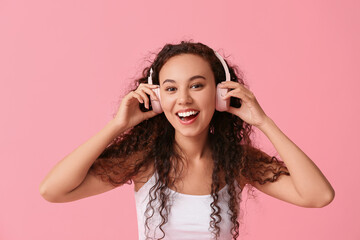 Happy young African-American woman in headphones on pink background