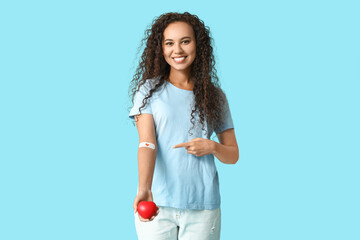 Young female African-American blood donor with heart pointing at applied medical patch on blue...