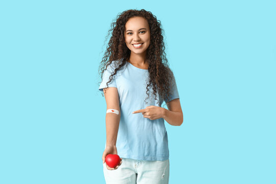 Young female African-American blood donor with heart pointing at applied medical patch on blue background
