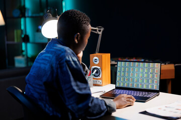 African American freelancer analyzes financial data, compares market trends, and trades online on personal computer. Concentrated black woman looking at laptop screen displaying forex trend values.