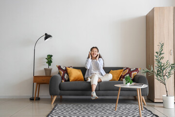 Obraz premium Young Asian woman in headphones sitting on black sofa at home