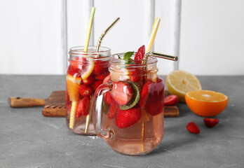 Mason jars of fresh infused water with strawberries, orange and lemon on grey table