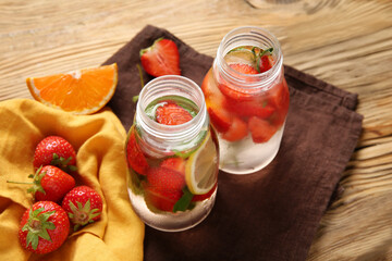 Bottles of infused water with strawberries and lemon on wooden background