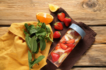Sports bottle of infused water with strawberries and lemon on wooden background