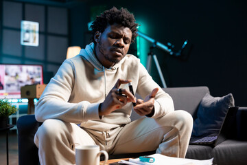 African american man clipping own finger using pulse oximeter, monitoring level of blood oxygen saturation and heart rate during annual checkup from comfort of his dimly lit home