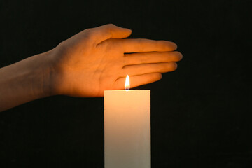 Hand with burning candle on black background. Day of Remembrance