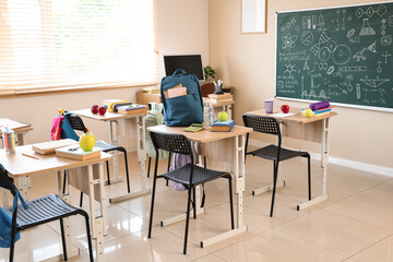 Desks with apples and school stationery in empty classroom