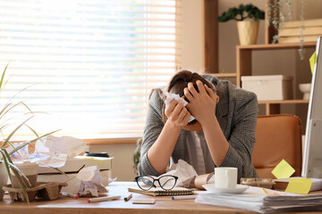 Stressed businesswoman with crumpled paper at messy table in office